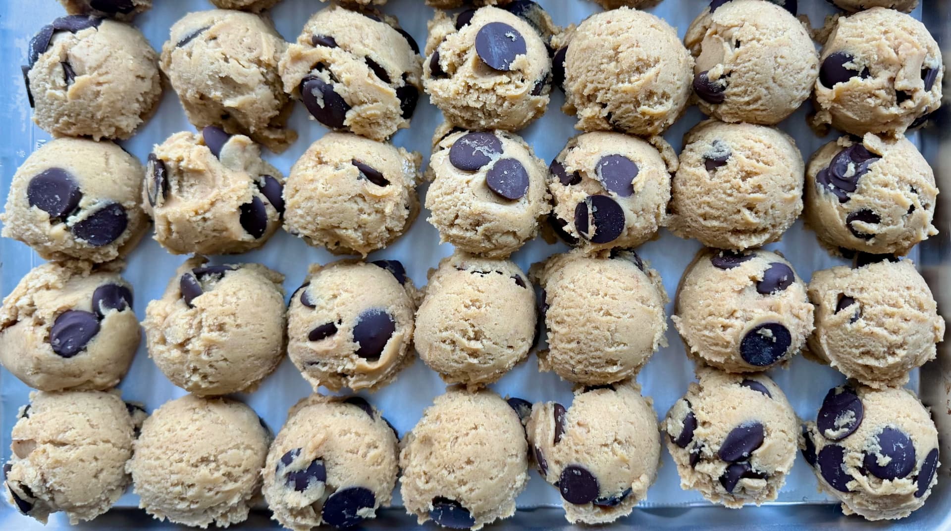A tray of scooped cookie dough portions with chocolate disks, ready for the freezer.