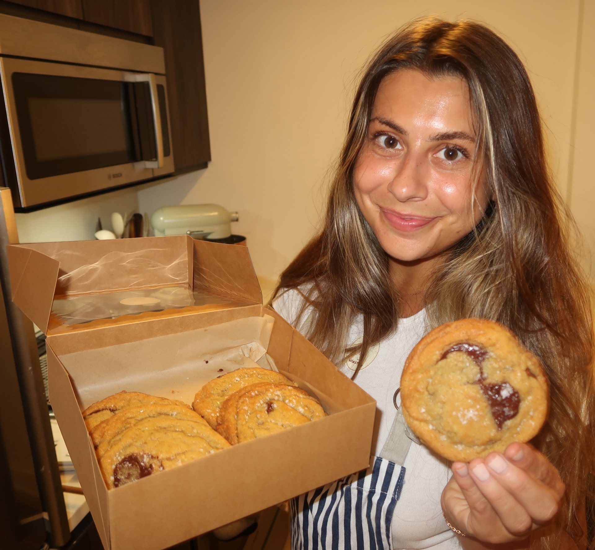Ashley in her kitchen holding a box of Treats by Winston cookies.