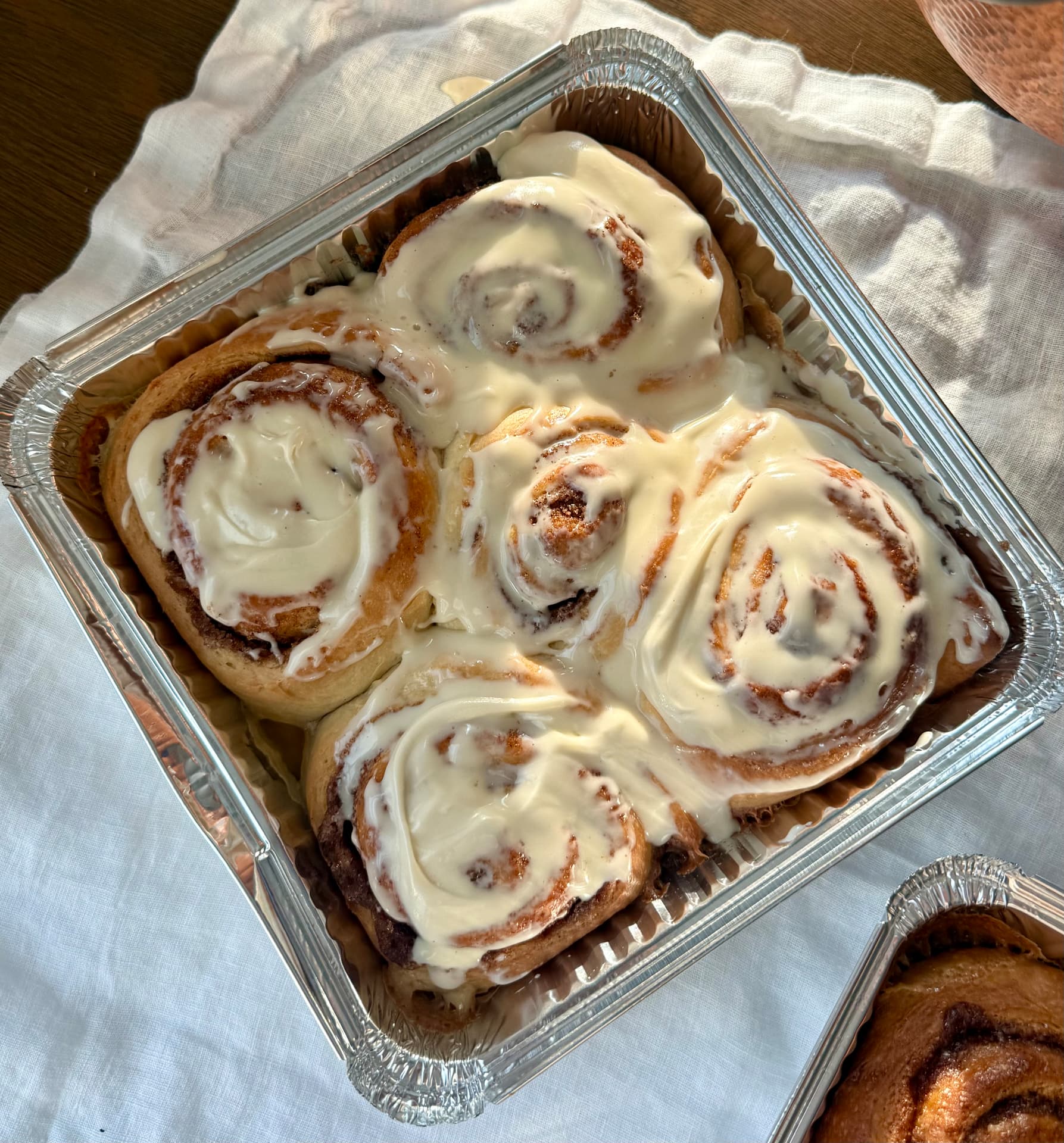 Four cinnamon buns with thick white icing in a foil baking tray.